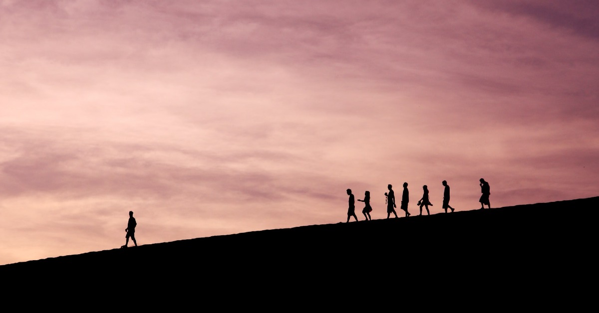 silhouette of people following a leader on a hill